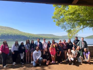 Student Group photo in front of a waterfront with hilly trees behind it
