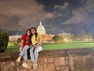 Two students taking a photo at night in front of Capital Hill in the distance